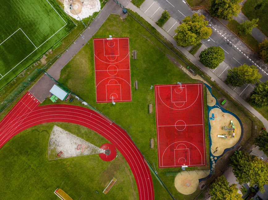 Aerial view of a sports complex with red basketball courts, a football field, and a running track.