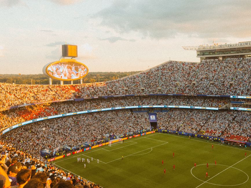 Aerial view of a packed soccer stadium during a lively match at sunset.