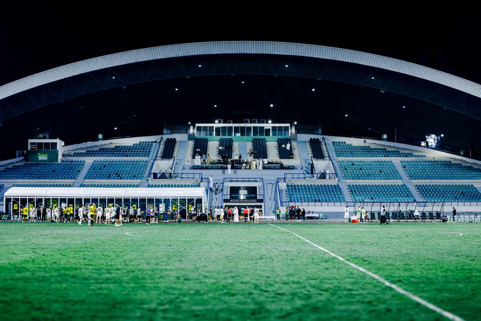 Panoramic view of a modern stadium during a night football match, vibrant and well-lit atmosphere.
