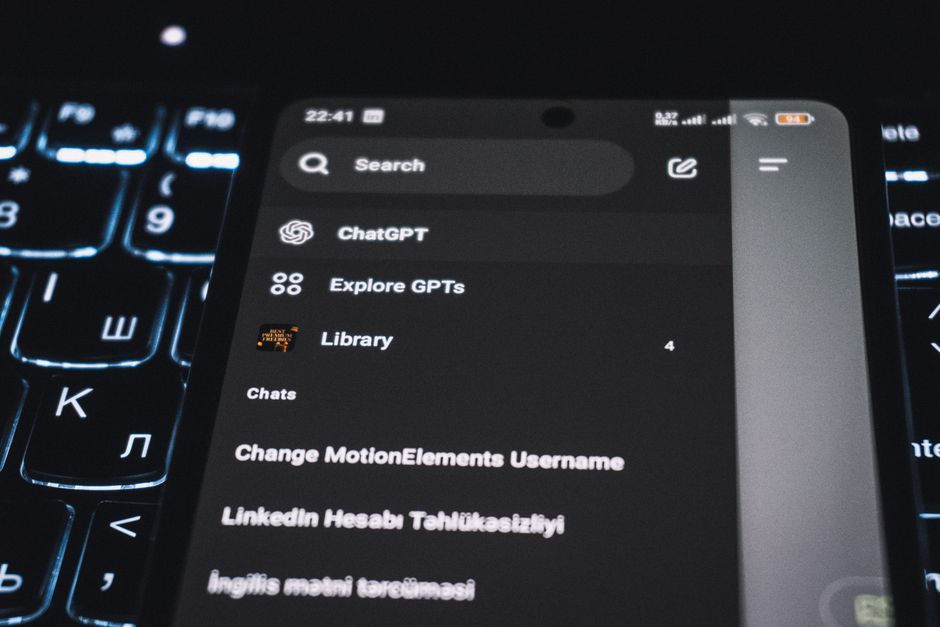 Close-up of a smartphone displaying a chat app interface with a backlit keyboard in the background.