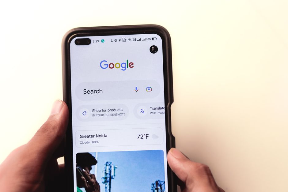 A close-up of a hand holding a smartphone with Google search displayed on the screen.